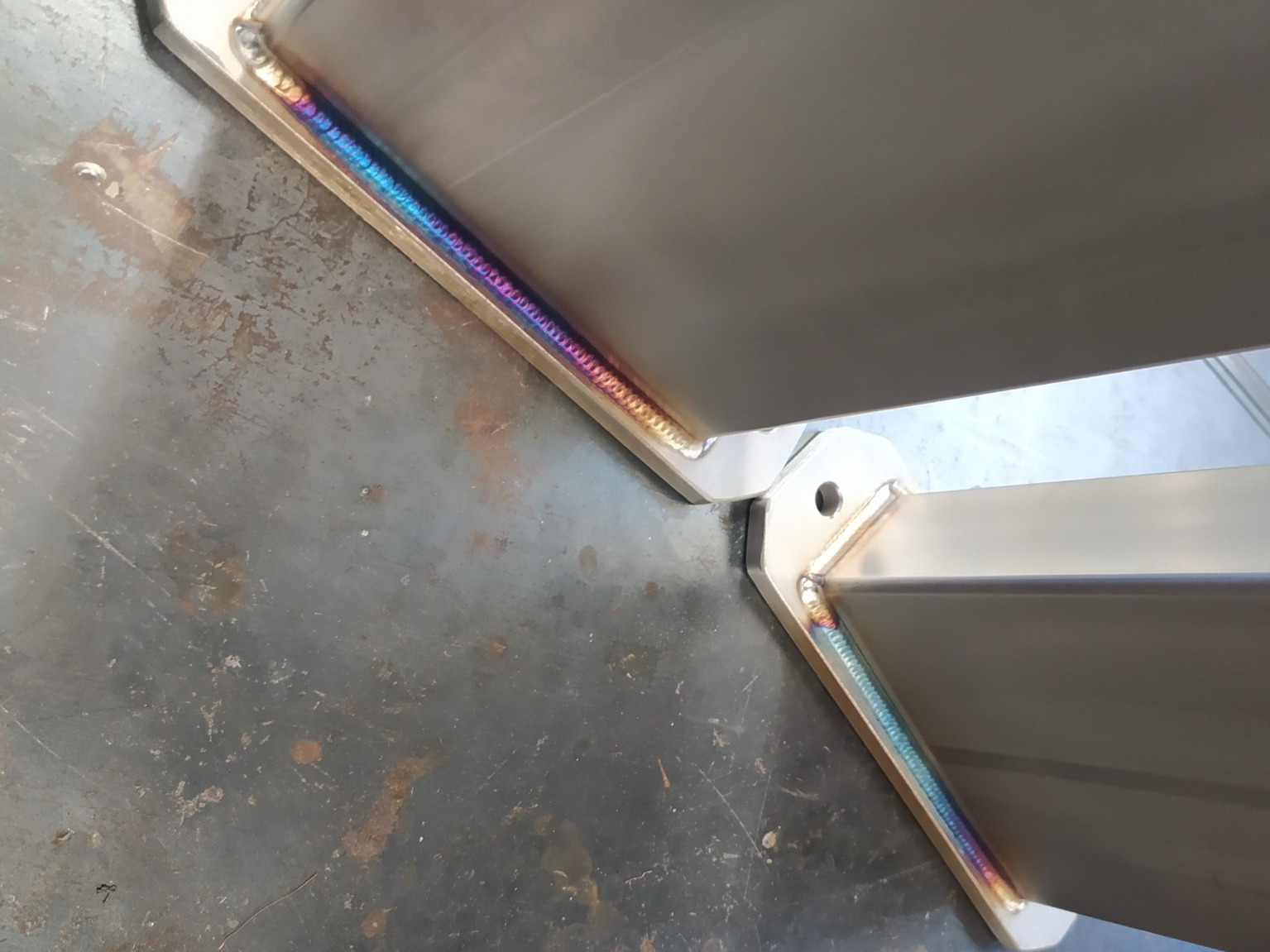 Szczegółowe ujęcie spawu łączącego elementy konstrukcji ze stali nierdzewnej, widoczne tęczowe zabarwienie spoiny.