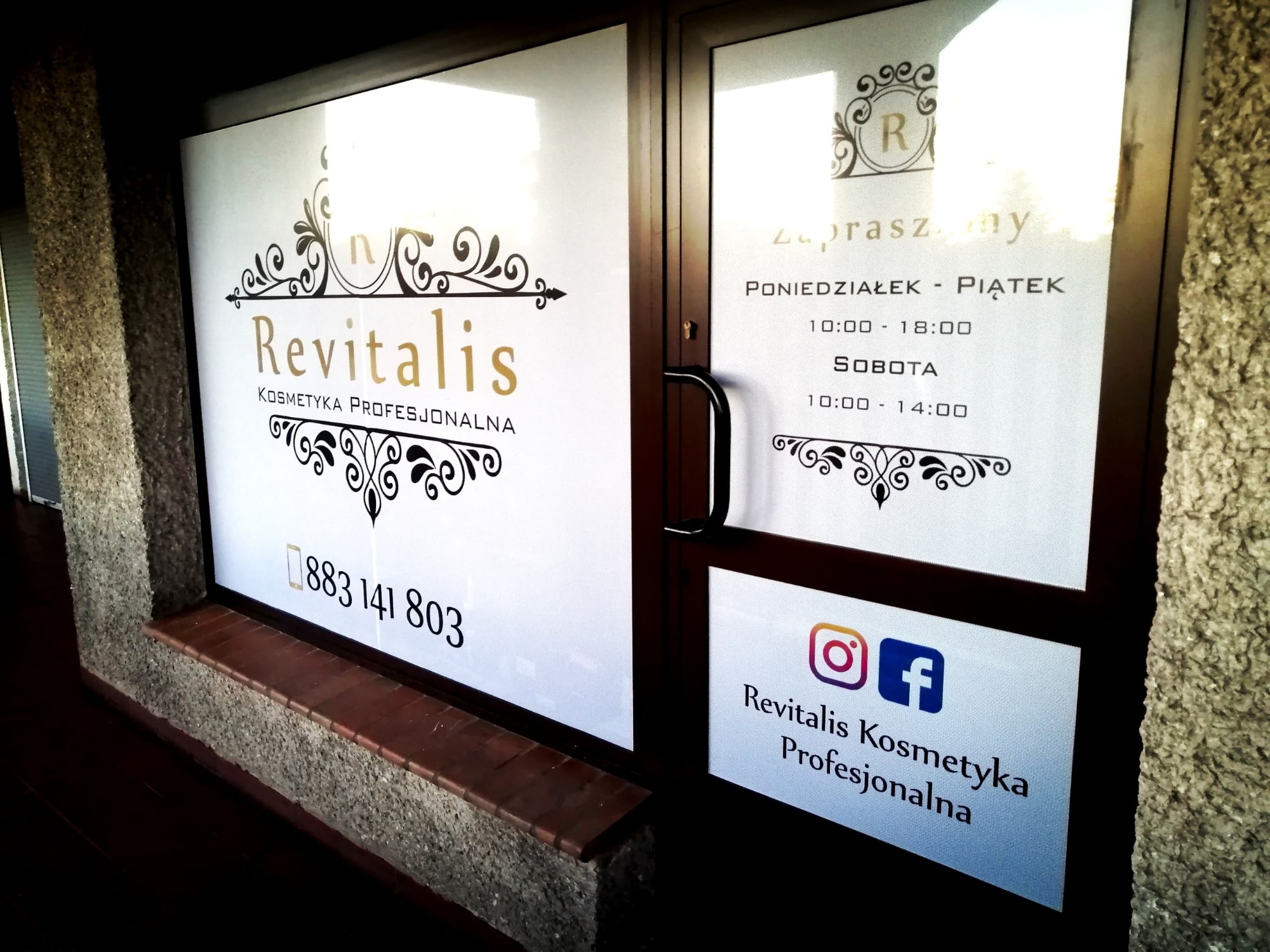Oklejona witryna salonu kosmetycznego z logo Revitalis, godzinami otwarcia i danymi kontaktowymi, w tym ikony Instagrama i Facebooka.