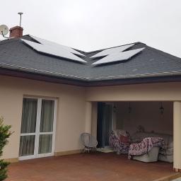 Fotowoltaika DARIUSZ JANISZEWSKI - Dom jednorodzinny z zamontowanymi panelami fotowoltaicznymi na dachu pokrytym czarną dachówką bitumiczną, widoczne również antena satelitarna i komin.