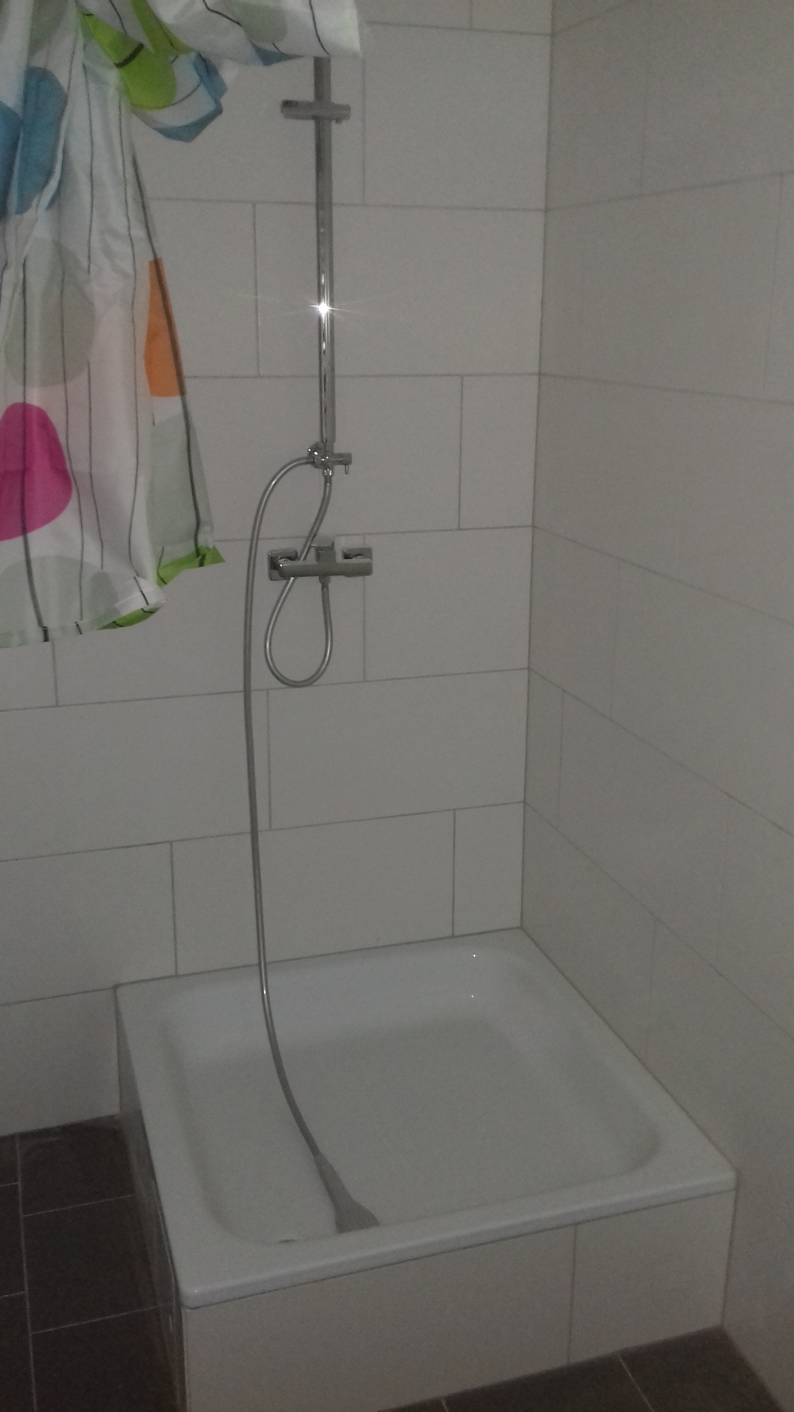 Biała kabina prysznicowa z panelami ściennymi, widoczna zasłona w kolorowe wzory i bateria prysznicowa.