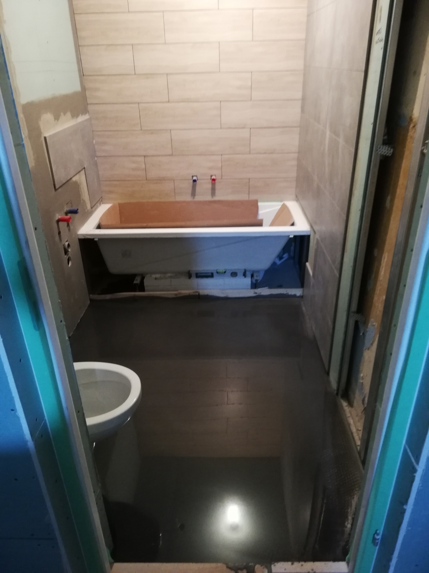 Wnętrze łazienki w trakcie remontu: położona glazura ścienna w odcieniach beżu, przygotowana do montażu wanna, widoczna instalacja wodna i częściowo ułożona podłoga.