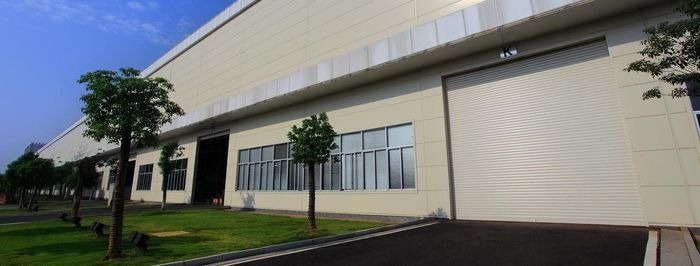 Duży budynek przemysłowy z zamkniętą, kremową bramą rolowaną, widok z zewnątrz w słoneczny dzień.