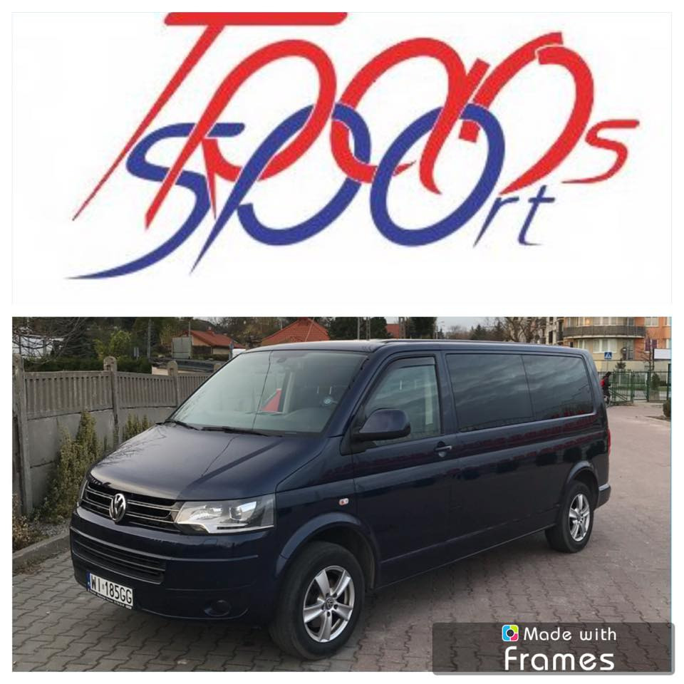 Granatowy Volkswagen Transporter z logo firmy transportowej w tle, zaparkowany na brukowanej ulicy w słoneczny dzień.