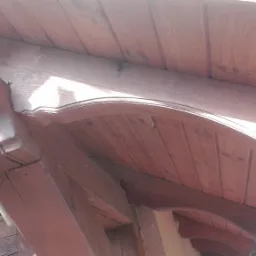 Drewniana konstrukcja dachu z rynną, widoczne elementy wykończeniowe i mocowania, brązowe zabarwienie drewna, ujęcie od dołu.