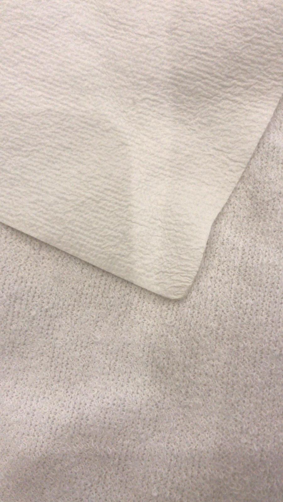 Dwa fragmenty białej tkaniny o różnej fakturze, gładka i dziergana, leżące obok siebie.