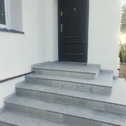 Wejście do domu z nową, granitową elewacją schod&oacute;w i świeżo pomalowaną elewacją w kolorze złamanej bieli.