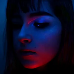 Portret kobiety w chłodnym, niebieskim oświetleniu z geometrycznym, czerwonym akcentem makijażu nad brwią i błyszczącym makijażem oczu.