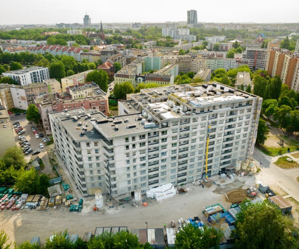 Wznoszenie wielopiętrowego budynku w Bezrzeczu, widok z lotu ptaka. Konstrukcja w stanie surowym, z widocznym żurawiem i materiałami budowlanymi.