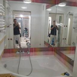 Misz masz - Łazienka w trakcie remontu: widoczna wanna z mozaiką, baterią i słuchawką prysznicową; w lustrze odbija się mężczyzna robiący zdjęcie i fragment pomieszczenia z drabiną.