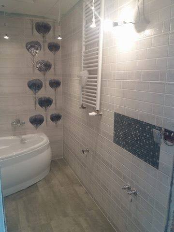 Jasna łazienka z wanną, grzejnikiem drabinkowym i mozaiką na ścianie, dekorowana wiszącymi ozdobami w kształcie serc.