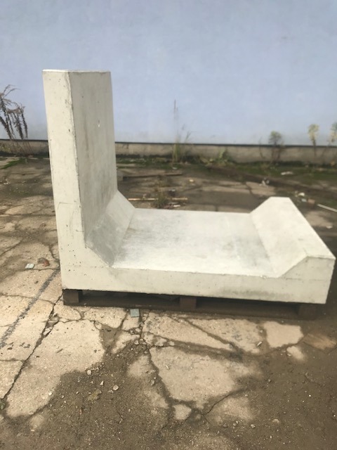Prefabrykowany element betonowy w kształcie litery U, umieszczony na palecie, widoczny na zewnątrz na tle szarej ściany.