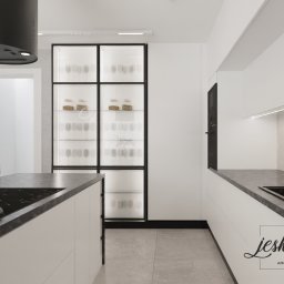 JESKA.DESIGN Magdalena Jerzewska - Minimalistyczna kuchnia z wyspą, czarnym okapem i przeszkloną witryną eksponującą szkło i naczynia, wykończona w bieli i szarości, oświetlona ledowymi listwami.