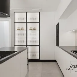 Minimalistyczna kuchnia z wyspą, czarnym okapem i przeszkloną witryną eksponującą szkło i naczynia, wykończona w bieli i szarości, oświetlona ledowymi listwami.