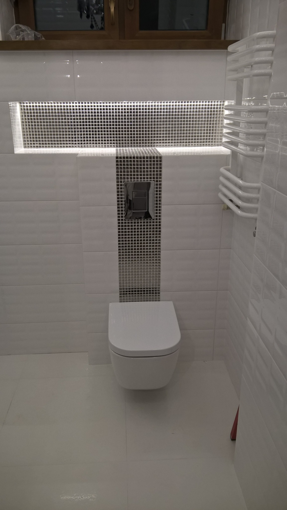 Nowoczesna łazienka z wiszącą toaletą, grzejnikiem drabinkowym i mozaiką w strefie spłuczki oraz wnęką z podświetleniem LED.