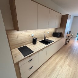 MARMAL - Nowoczesna kuchnia z drewnianymi akcentami: beżowe szafki, czarny zlew i płyta indukcyjna, drewniany blat i podłoga. Minimalistyczny design z oświetleniem podszafkowym.