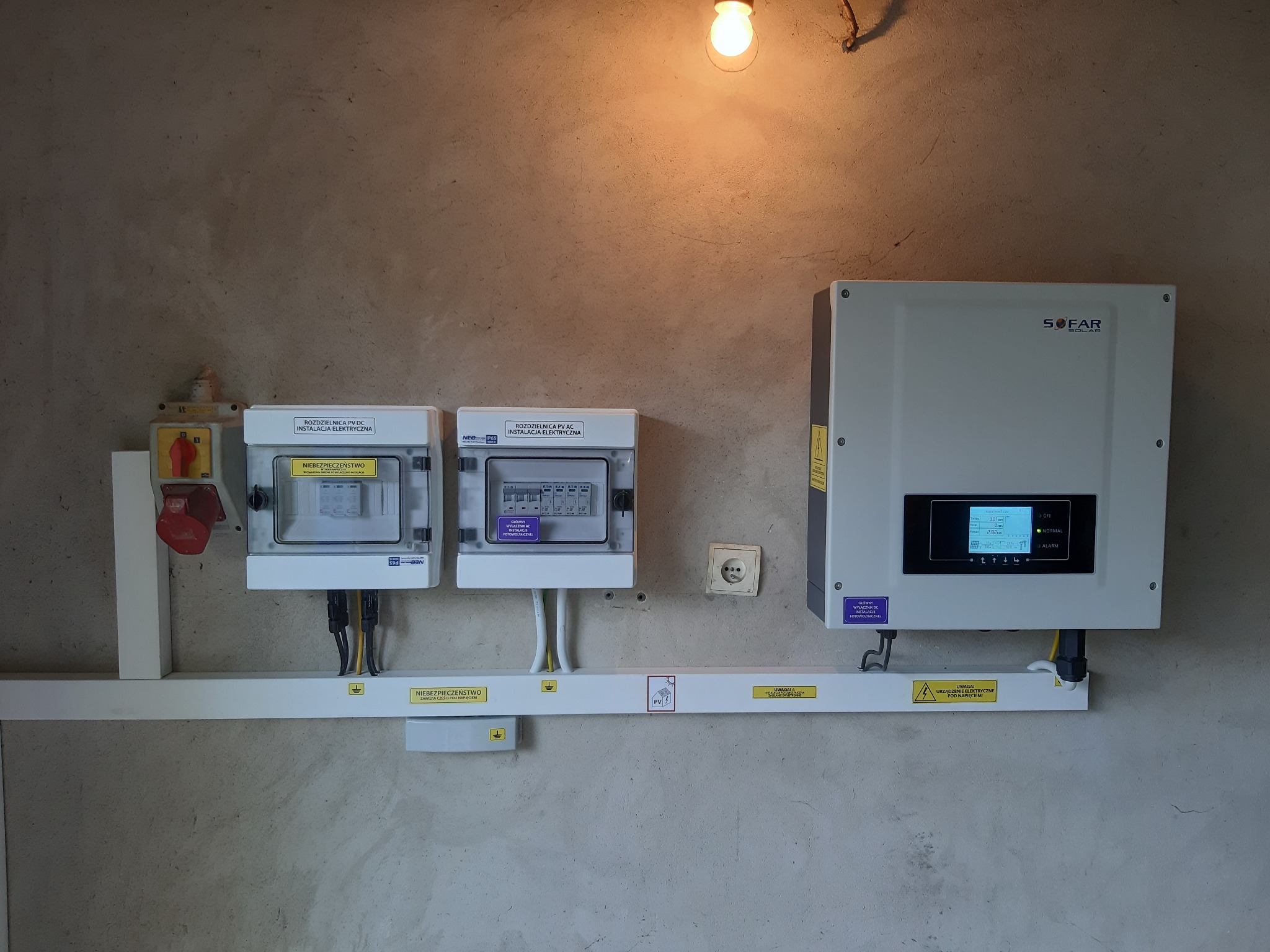 Rozdzielnice PV DC i AC, falownik Sofar Solar zamontowane na ścianie z widocznymi przewodami i oznaczeniami ostrzegawczymi, oświetlone żarówką