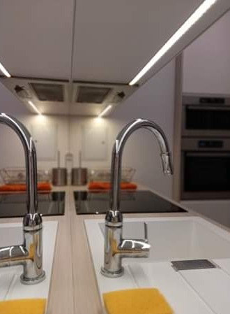 Błyszczące baterie kuchenne nad białymi zlewozmywakami w minimalistycznej kuchni z oświetleniem LED pod szafkami.