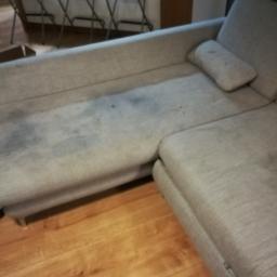 ECO PURE - Szara, narożna kanapa z widocznymi plamami na siedzisku, ukazana na tle drewnianej podłogi i krzeseł.