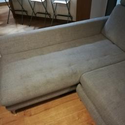 ECO PURE - Szara, narożna kanapa z widocznymi plamami na tapicerce, ustawiona na drewnianej podłodze, w tle krzesła barowe.