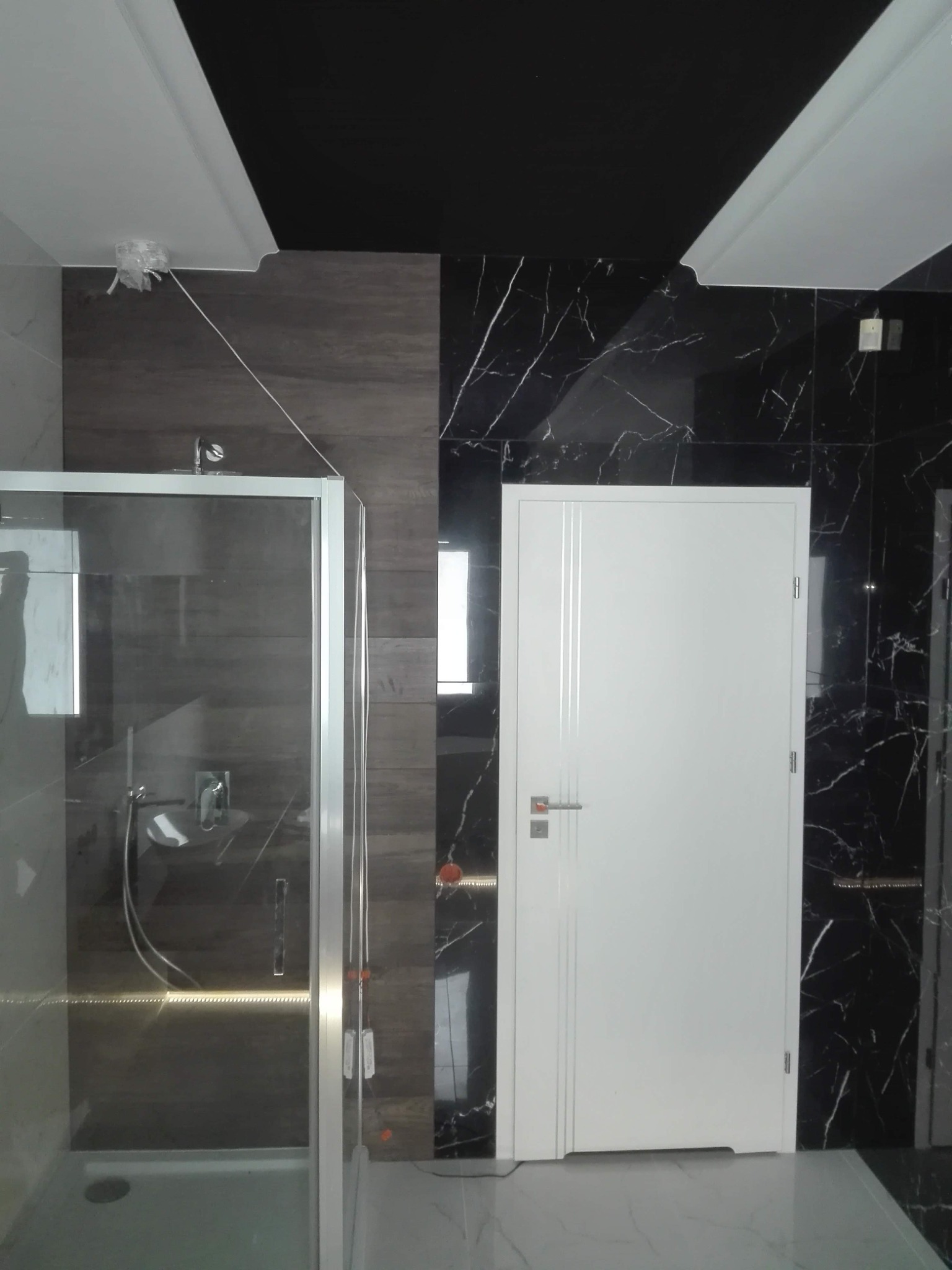 Nowoczesna łazienka z kabiną prysznicową, ciemnymi płytkami imitującymi marmur i białą stolarką drzwiową z trzema pionowymi frezami.