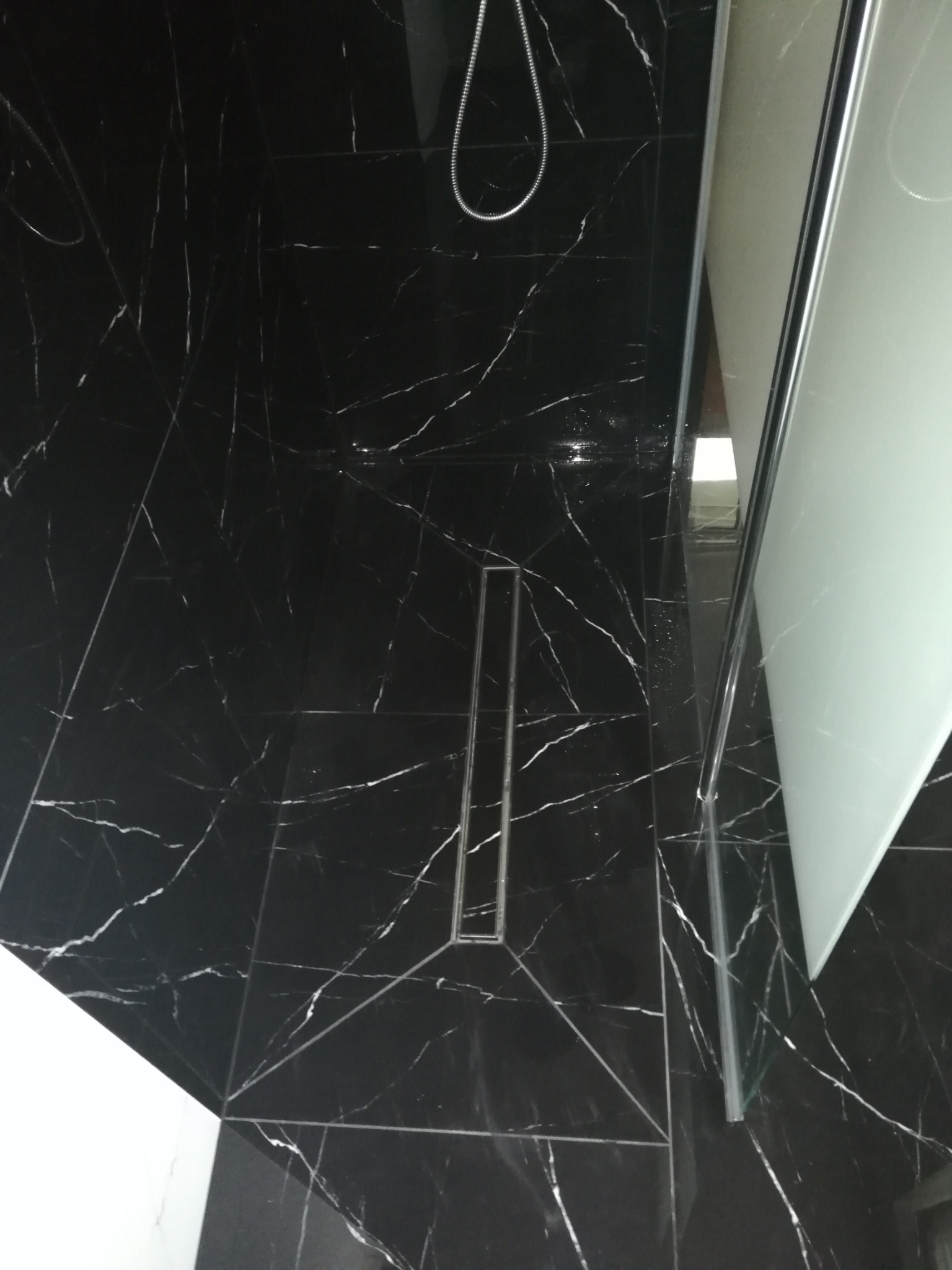 Kabina prysznicowa z czarnymi płytkami imitującymi marmur i odpływem liniowym w podłodze.