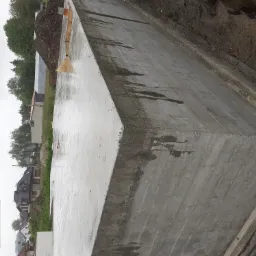 Wylany, mokry betonowy fundament z widocznymi śladami szalunku, obok pryzma ziemi, w tle zabudowa jednorodzinna i pochmurne niebo.