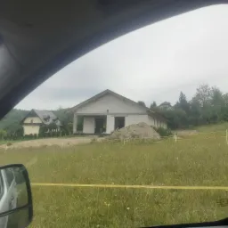 Surowy stan domu w trakcie budowy, widok z wnętrza samochodu przez szybę, z widocznymi elementami wnętrza pojazdu.