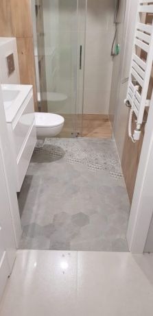 Nowoczesna łazienka z szarą, heksagonalną mozaiką na podłodze, kabiną prysznicową ze szklanymi drzwiami i białą umywalką z szafką.