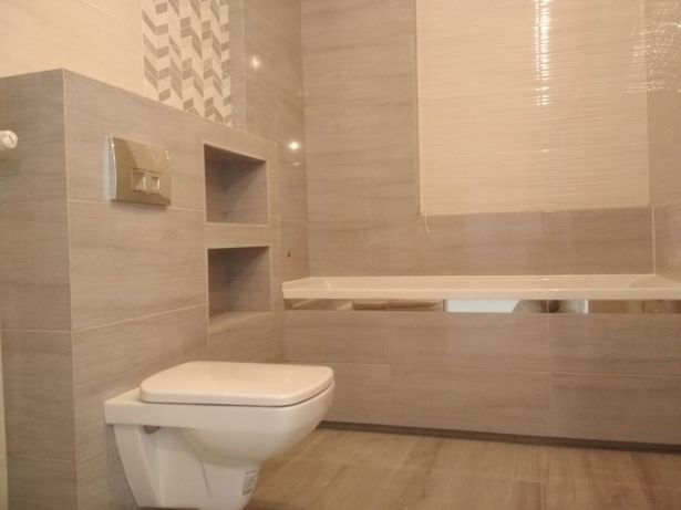 Wykończona łazienka w odcieniach beżu i szarości z wiszącą toaletą, wnękami w ścianie i dekoracyjnym wzorem płytek nad spłuczką.