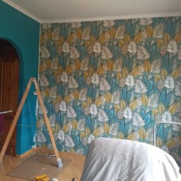 Usługi remontowo - wykończeniowe Grzegorz Myśliwiec - Pokój po tapetowaniu: ściana w liście w odcieniach błękitu, bieli i złota, drabina drewniana oparta o ścianę, fragment turkusowej ściany obok łuku drzwiowego