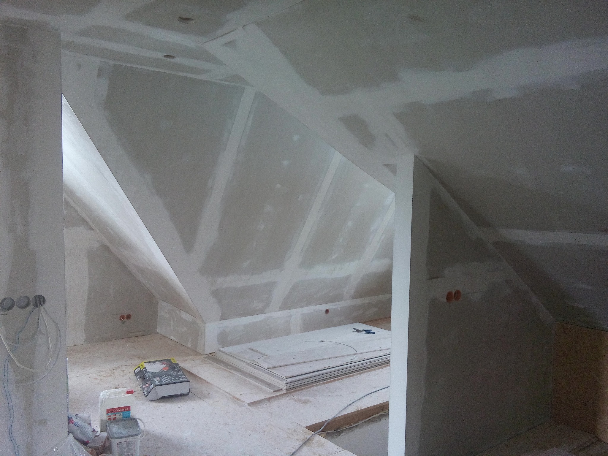 Poddasze w trakcie prac wykończeniowych: ściany i sufit pokryte płytami gipsowo-kartonowymi, widoczne szpachlowanie łączeń, na podłodze leżą płyty, wiadro z gruntem i narzędzia.