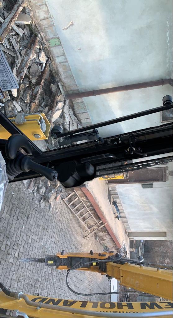 Żółta maszyna z wiertłem hydraulicznym podczas wyburzania ściany w Wodzisławiu Śląskim, widok z góry na gruz i zniszczony budynek.