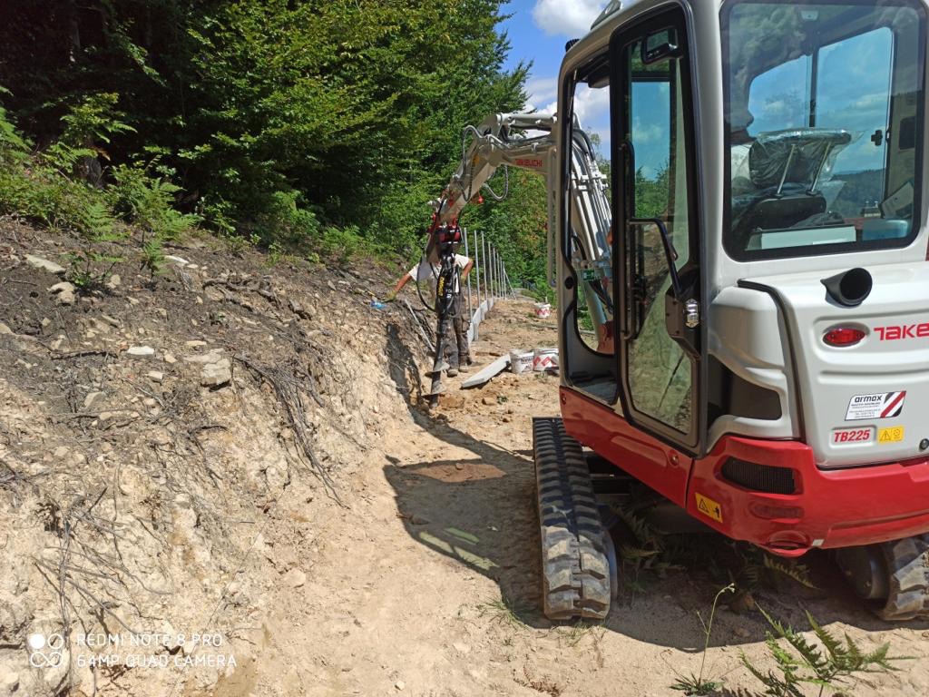 Mini koparka Takeushi TB225 z operatorem w trakcie pracy na zboczu, przygotowanie terenu pod instalacje, widoczne wykopane rury.