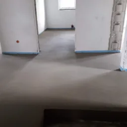 Świeżo wylana, gładka posadzka jastrychowa w surowym wnętrzu, z widocznymi fragmentami zabezpieczeń na ścianach i otworami na instalacje elektryczne.