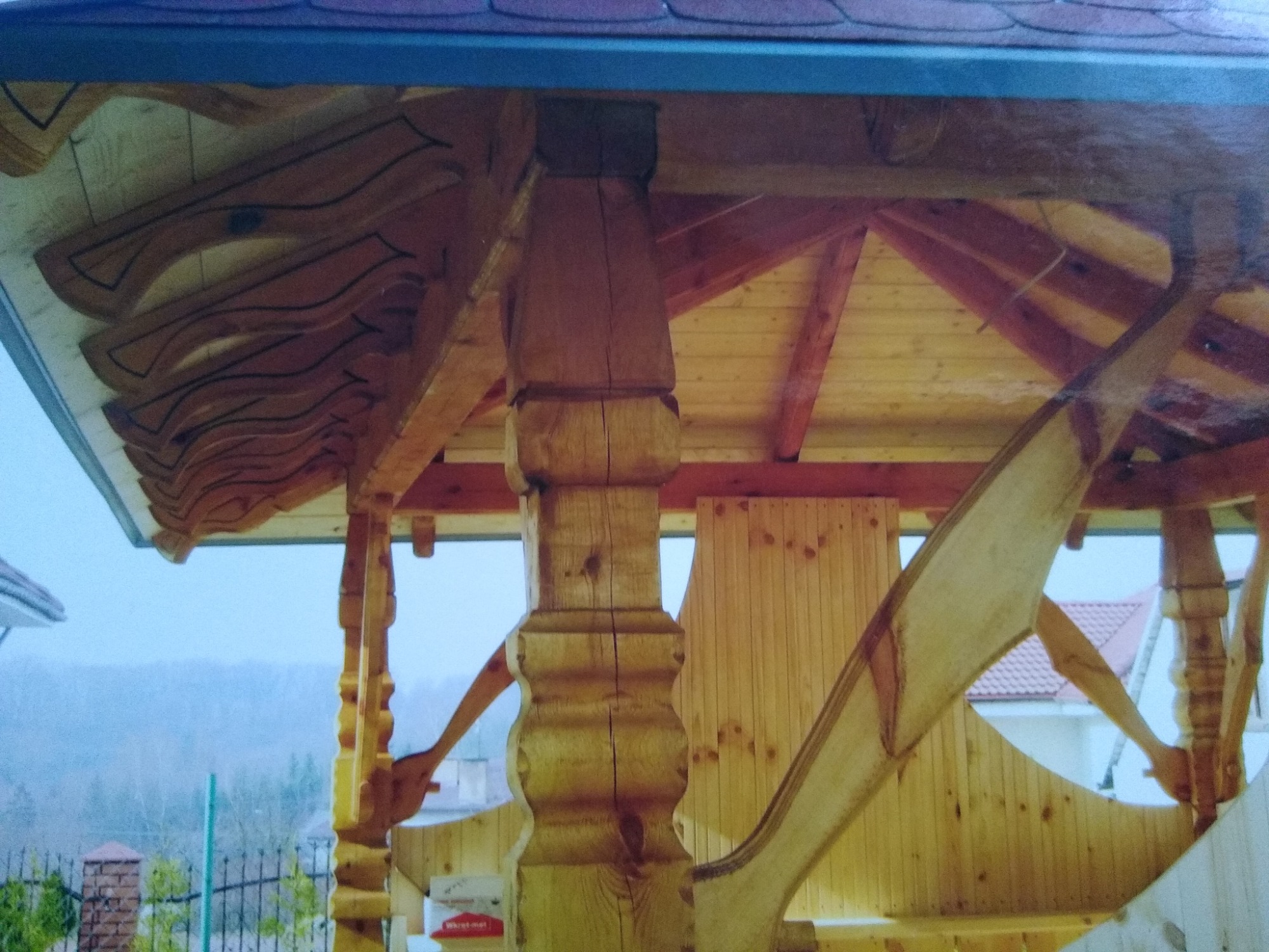 Drewniana konstrukcja altany z dekoracyjnymi elementami i widocznym dachem w tle krajobraz z zalesionym wzgórzem.