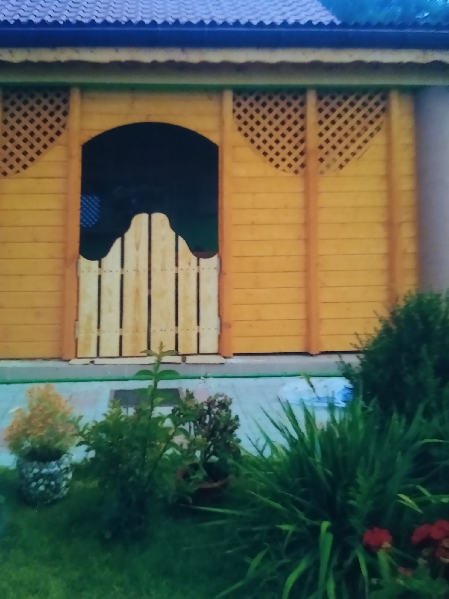 Drewniana pergola z ażurowymi ścianami i ozdobną bramką, otoczona zielenią w Świeciu.