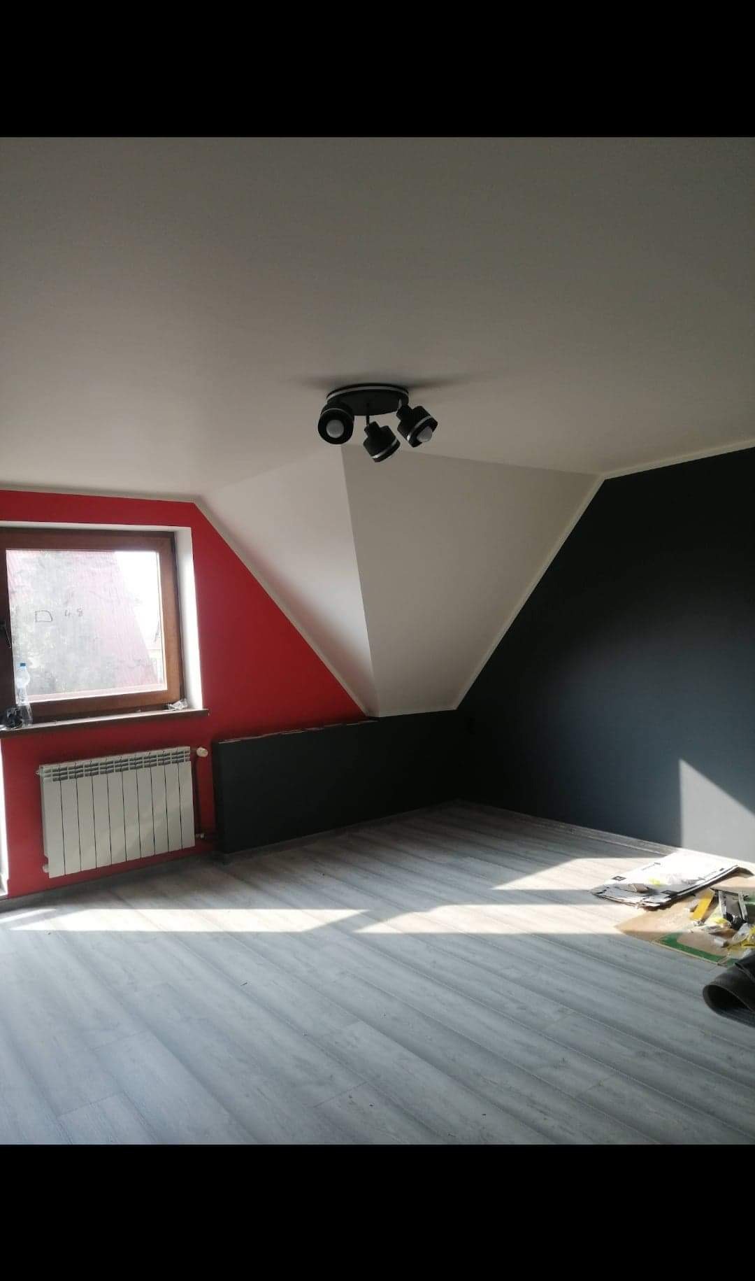 Pokój na poddaszu po remoncie: ściany pomalowane na czerwono, czarno i biało, drewniana podłoga, okno z grzejnikiem, nowoczesne oświetlenie sufitowe.
