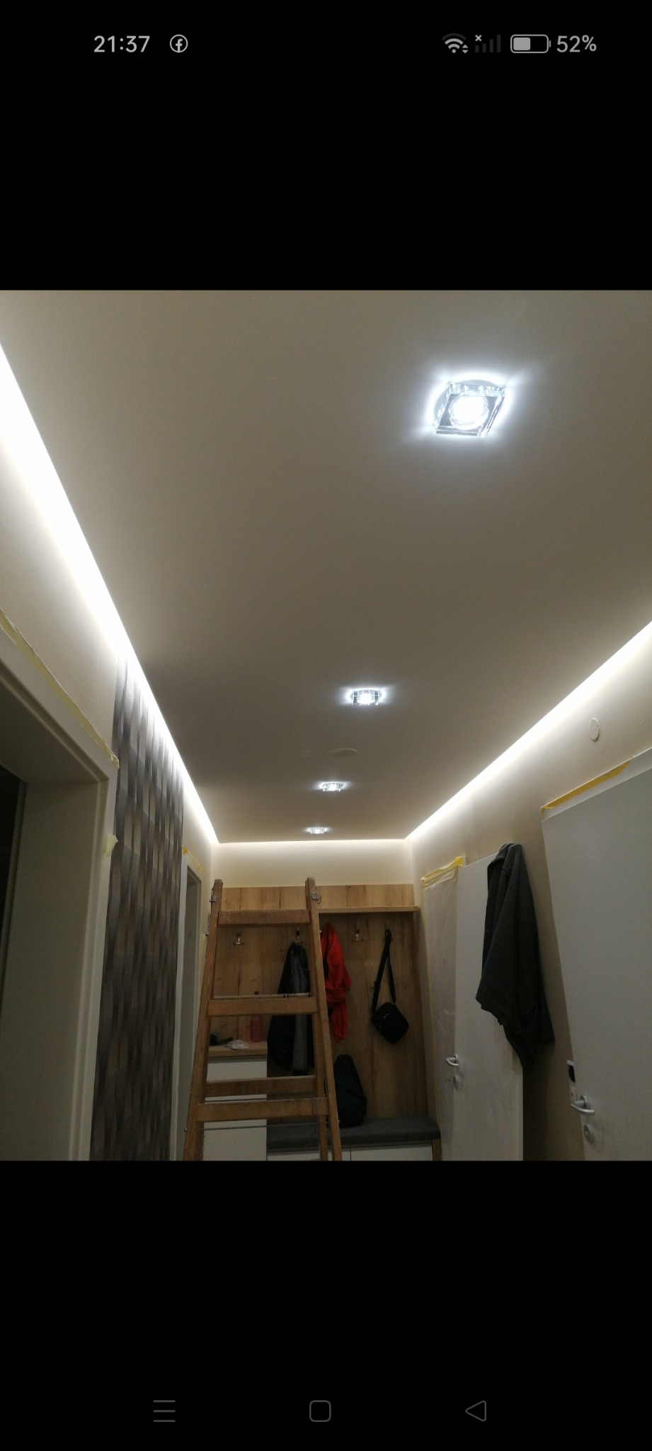 Korytarz w trakcie remontu z oświetleniem LED pod sufitem, drewnianą drabina opartą o ścianę i wnęką z wieszakami.