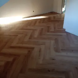 Ułożona podłoga z paneli w jodełkę angielską, widok z góry, jasne drewno, świeżo po montażu, widoczne ściany i fragment drzwi.