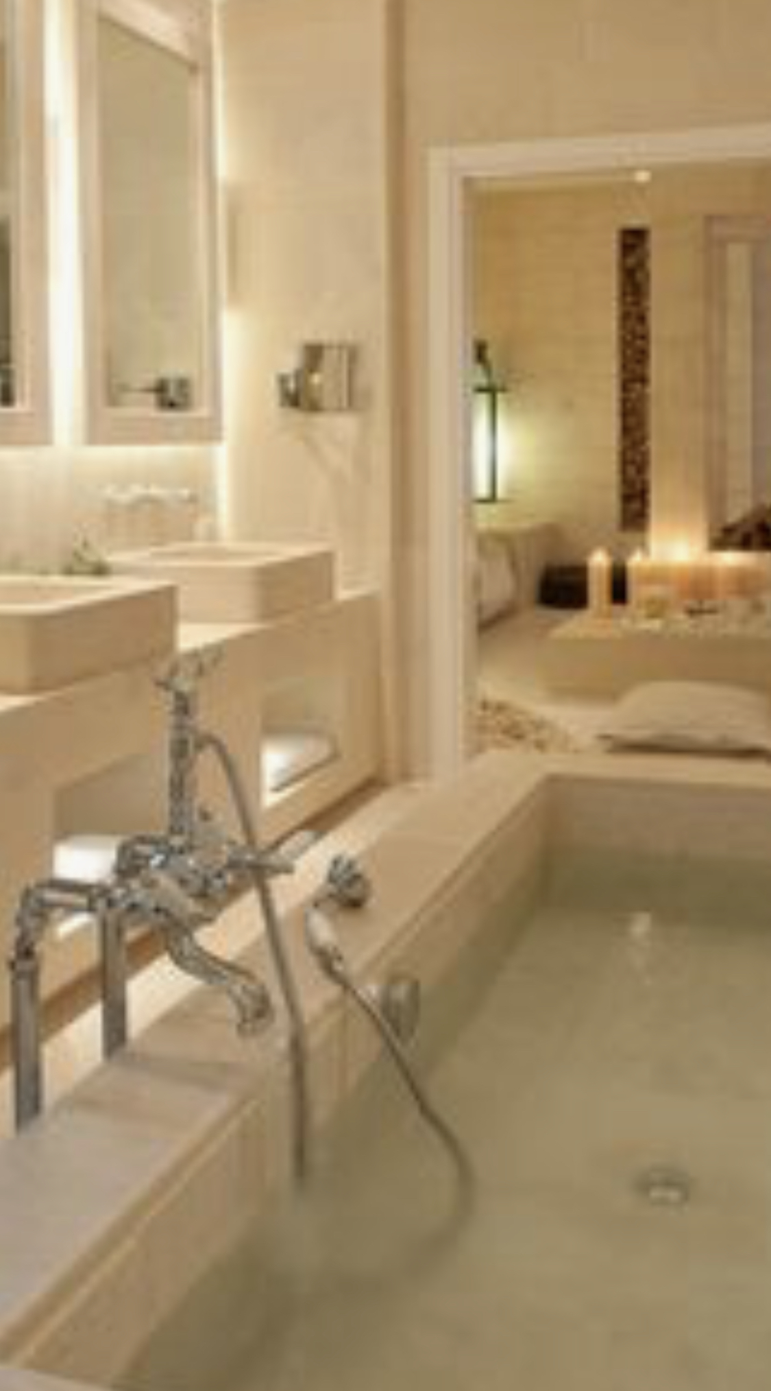 Jasna łazienka z wanną wypełnioną wodą, ozdobna bateria wannowa w stylu retro, umywalki wbudowane w kamienny blat, w tle sypialnia z zapalonymi świecami.