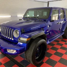 Błyszczący, granatowy Jeep Wrangler po umyciu, z widoczną strukturą opon i odbiciem światła w karoserii, na podłodze w czarno-czerwoną szachownicę.