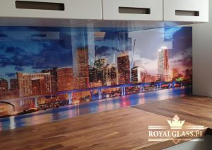Szklany panel ścienny w kuchni z motywem nocnej panoramy miasta, odbijającej się w wodzie, zamontowany między blatem a szafkami, z widocznym logo firmy Royal Glass w prawym dolnym rogu.