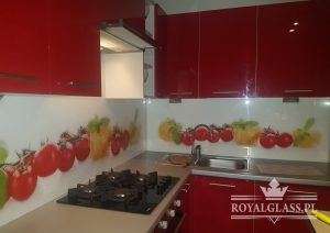 Szklany panel kuchenny z motywem warzyw, zamontowany nad blatem i kuchenką gazową w czerwonej kuchni, widoczny okap.