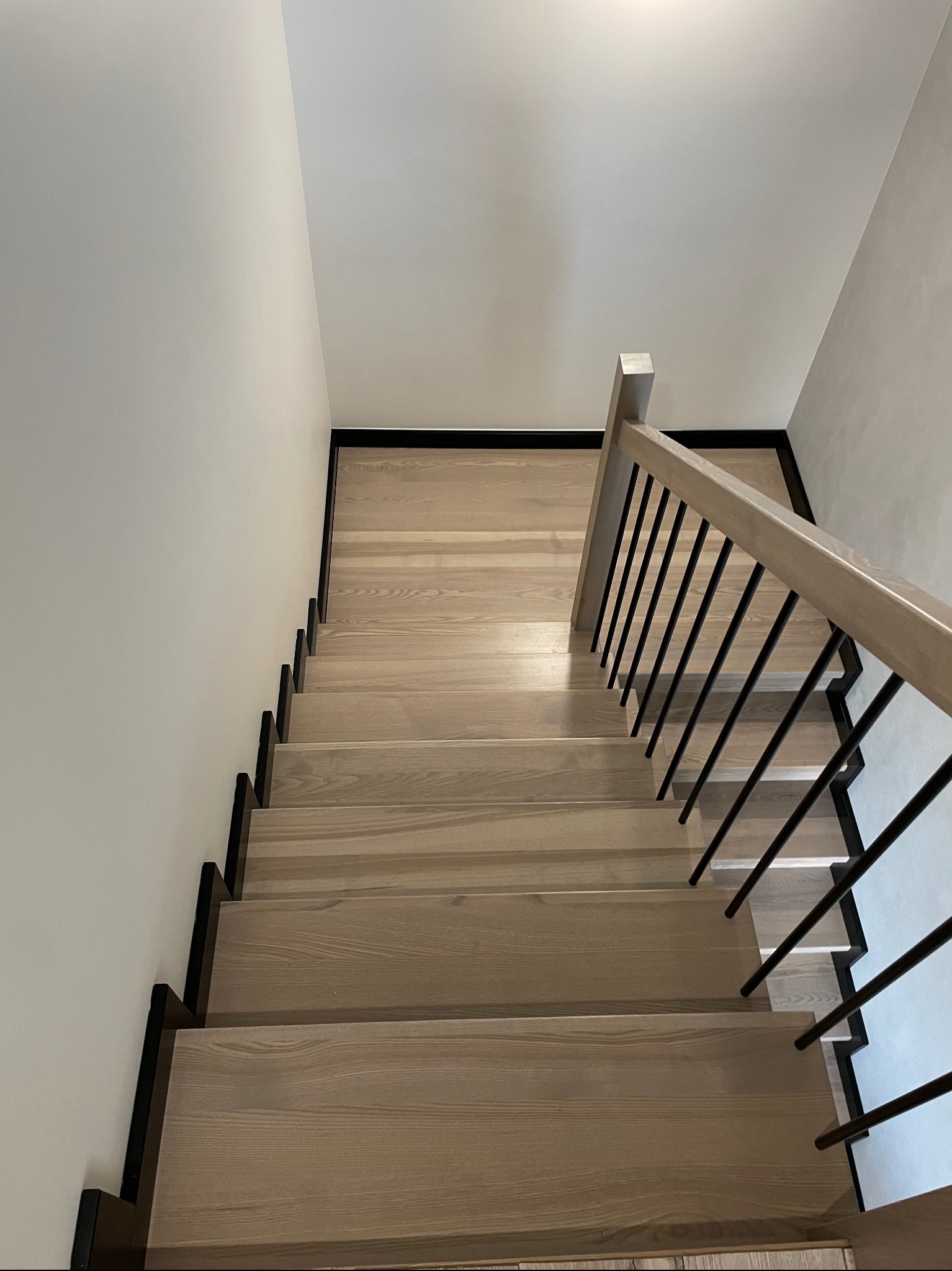 Widok z góry na jasne stopnie z ciemnymi podstopnicami i metalową balustradą, minimalistyczny design.