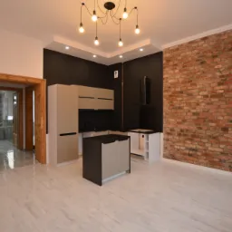 Nowoczesna kuchnia z ceglaną ścianą, beżowymi szafkami i marmurową podłogą, widok na łazienkę przez drewnianą framugę drzwi.