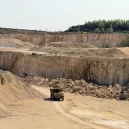 Panoramiczny widok kopalni odkrywkowej w okolicach Małogoszcza z ciężarówką na tle hałd urobku i pracującą koparką.