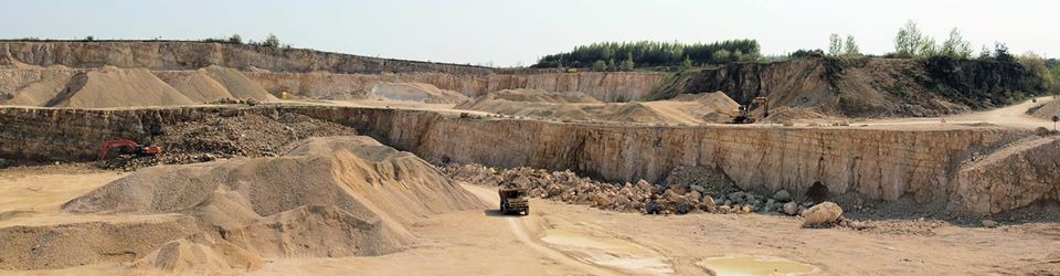 Panoramiczny widok kopalni odkrywkowej w okolicach Małogoszcza z ciężarówką na tle hałd urobku i pracującą koparką.