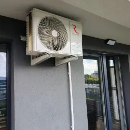 Klimatyzator Rotenso zamontowany na szarej ścianie balkonu, widoczne wsporniki montażowe i rurka odprowadzająca skropliny.