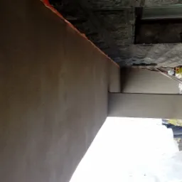 Świeżo otynkowana ściana zewnętrzna budynku w Bielsko-Białej, widoczne ślady prac murarskich i przygotowania do dalszych etapów wykończeniowych, zarys kostki brukowej na podłożu.