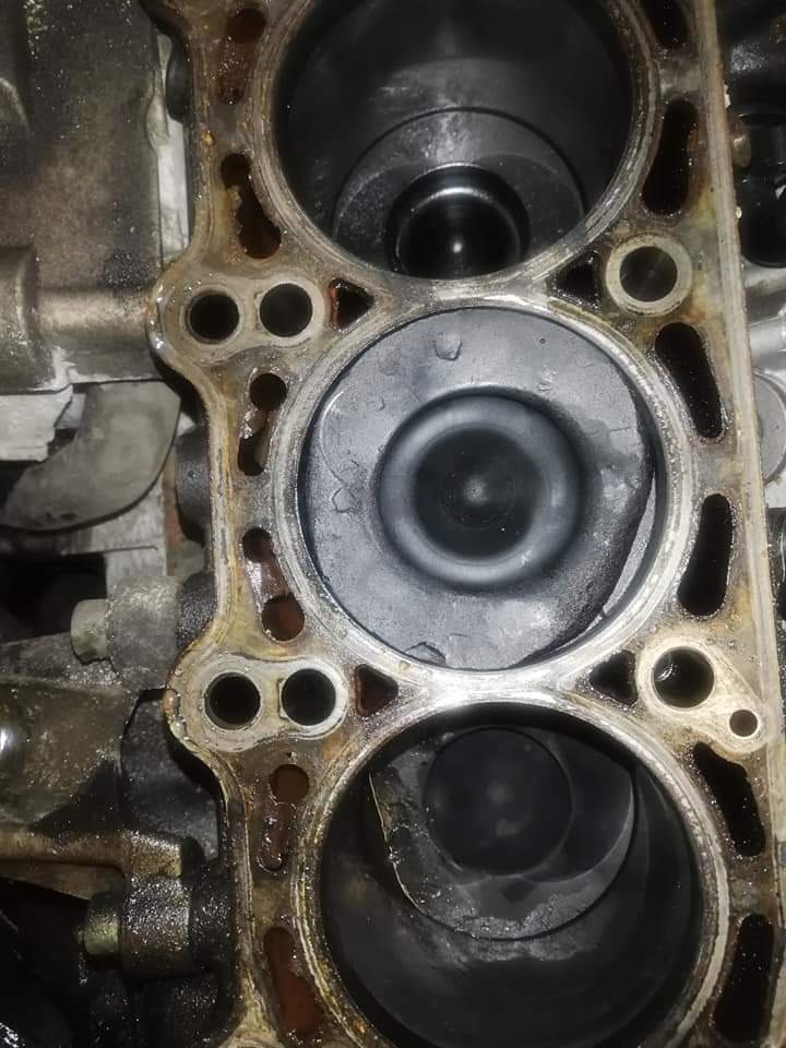 Blok silnika samochodowego z widocznymi cylindrami i tłokami, ślady oleju i zabrudzenia, widoczne ślady korozji na krawędziach.